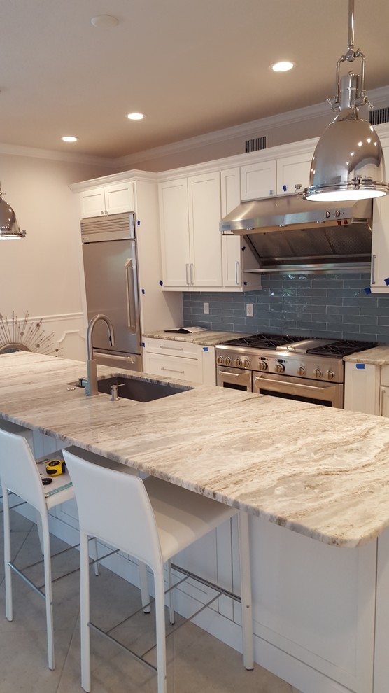 Photo of a large beach style l-shaped open plan kitchen in Tampa with an undermount sink, shaker cabinets, white cabinets, granite benchtops, blue splashback, glass tile splashback, stainless steel appliances, porcelain floors and with island.