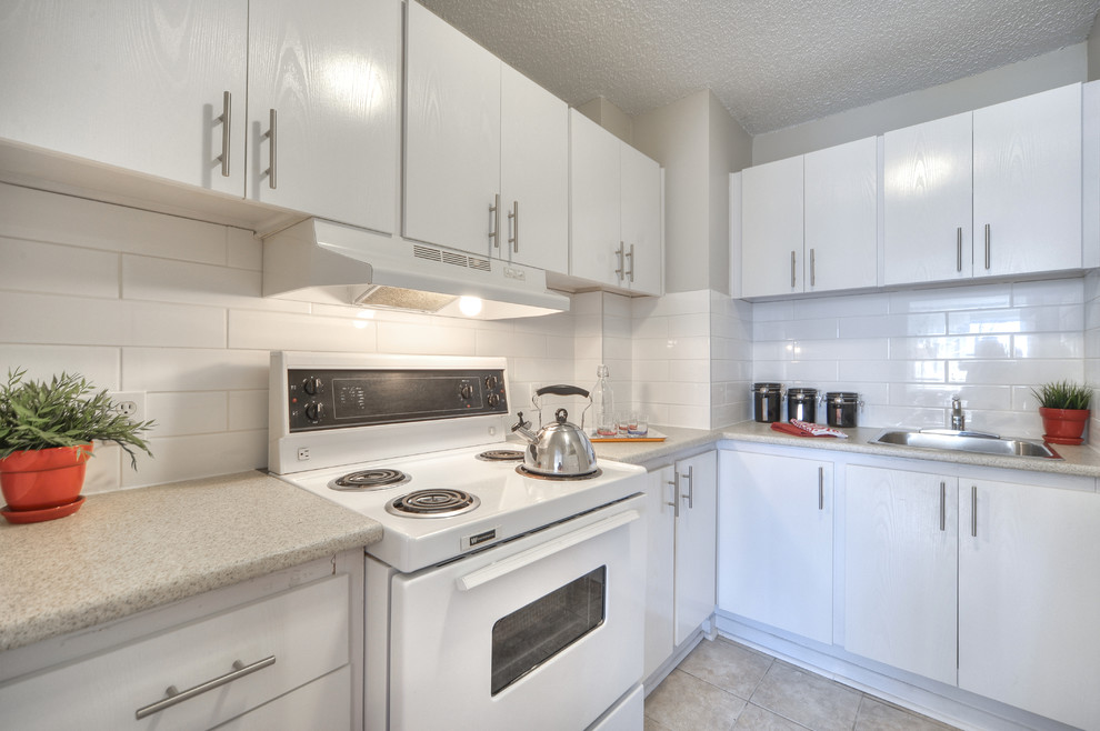 Design ideas for a small contemporary u-shaped separate kitchen in Montreal with a drop-in sink, flat-panel cabinets, white cabinets, laminate benchtops, white splashback, ceramic splashback, white appliances and ceramic floors.
