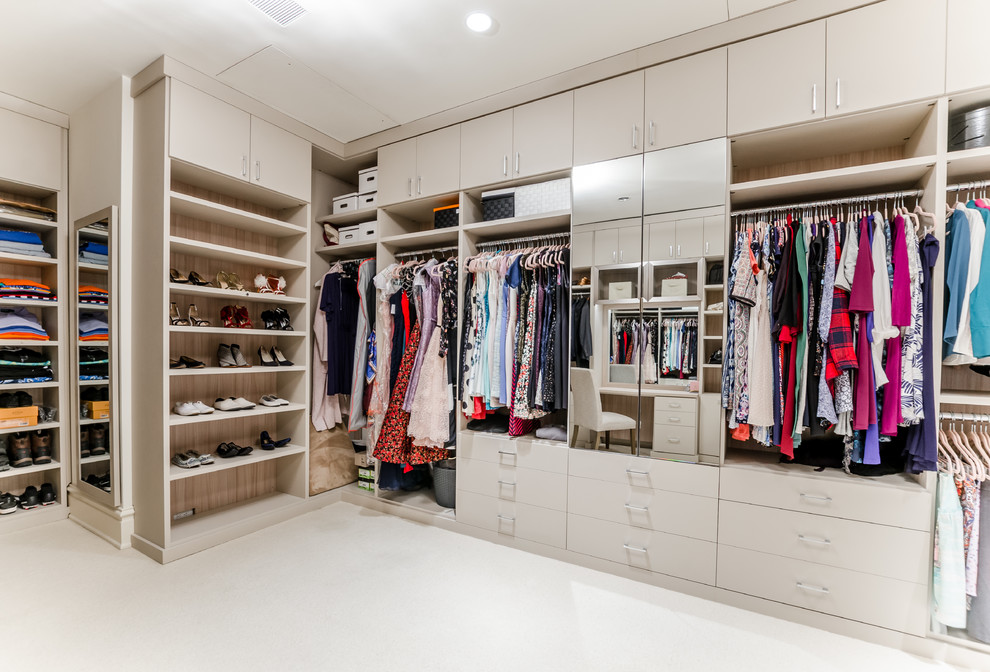 Modern gender-neutral walk-in wardrobe in New York with open cabinets, beige cabinets, carpet and beige floor.