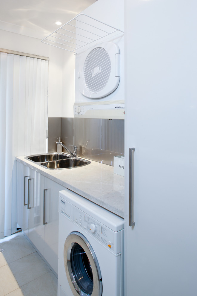 Design ideas for a small contemporary galley dedicated laundry room in Perth with a drop-in sink, flat-panel cabinets, white cabinets, laminate benchtops, yellow walls, ceramic floors and a stacked washer and dryer.