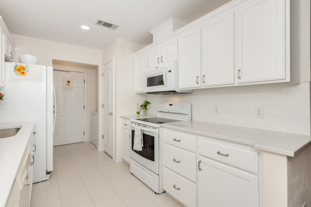 Photo of a traditional eat-in kitchen in Austin with recessed-panel cabinets, white cabinets, quartz benchtops, white splashback, subway tile splashback, no island and white benchtop.