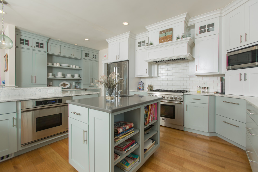 Photo of a beach style u-shaped kitchen in Providence with recessed-panel cabinets, blue cabinets, white splashback, subway tile splashback, stainless steel appliances, medium hardwood floors, with island and brown floor.