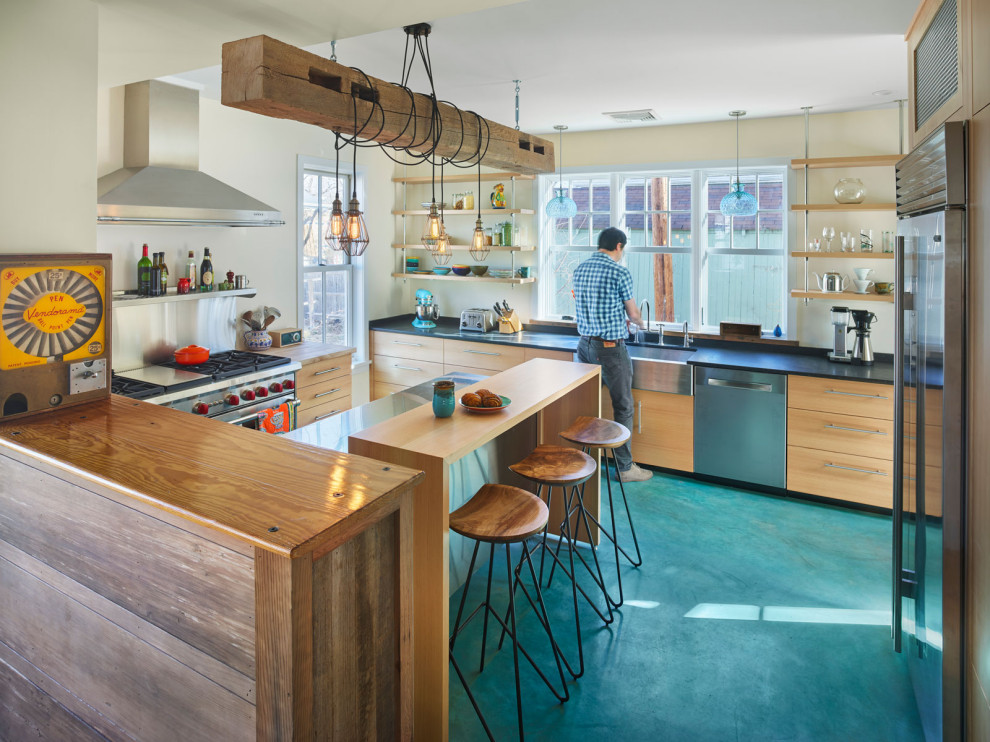 Design ideas for a large eclectic u-shaped kitchen in New York with a farmhouse sink, flat-panel cabinets, light wood cabinets, grey splashback, stainless steel appliances, concrete floors, a peninsula, blue floor and black benchtop.