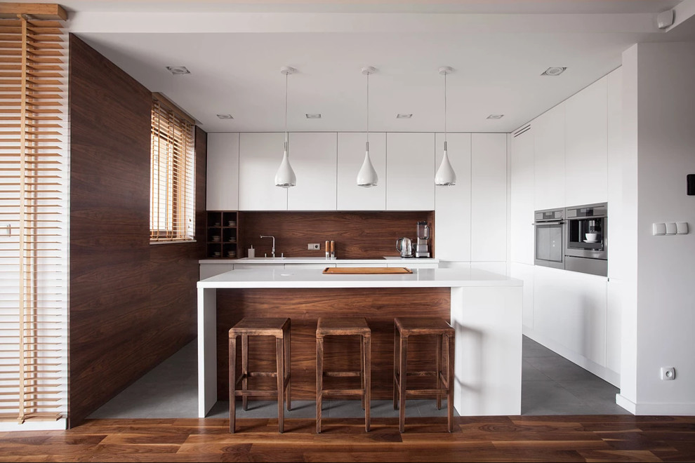 Mid-sized modern l-shaped kitchen in Los Angeles with flat-panel cabinets, white cabinets, timber splashback, stainless steel appliances, with island, an undermount sink, quartz benchtops, brown splashback, grey floor and white benchtop.