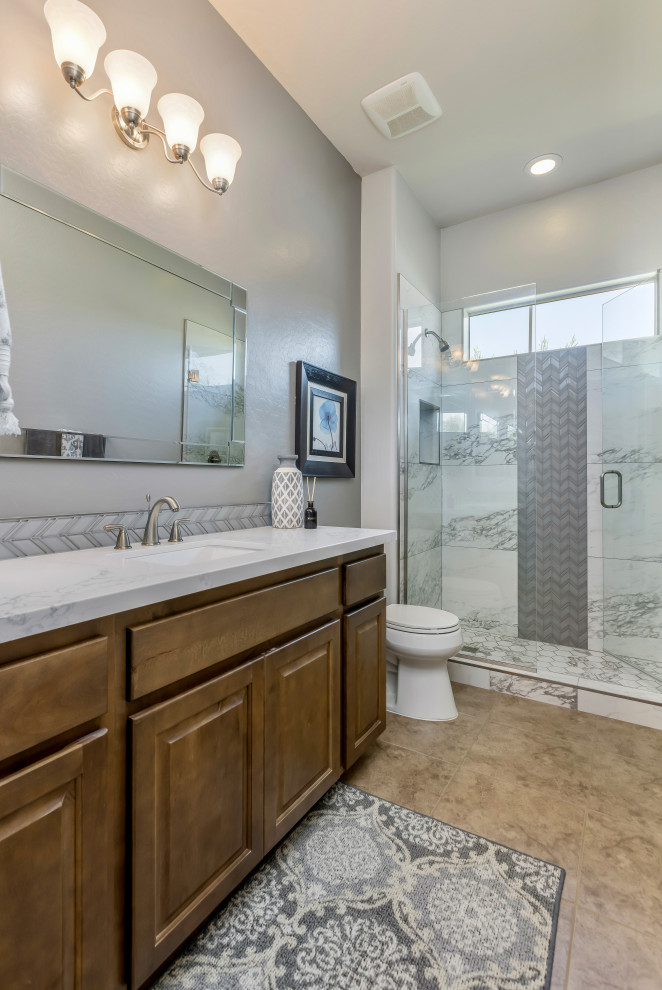 This is an example of a mid-sized transitional master bathroom in Phoenix with shaker cabinets, medium wood cabinets, an alcove shower, a two-piece toilet, white tile, porcelain tile, grey walls, porcelain floors, an undermount sink, engineered quartz benchtops, brown floor, a hinged shower door, white benchtops, a niche, a single vanity and a built-in vanity.
