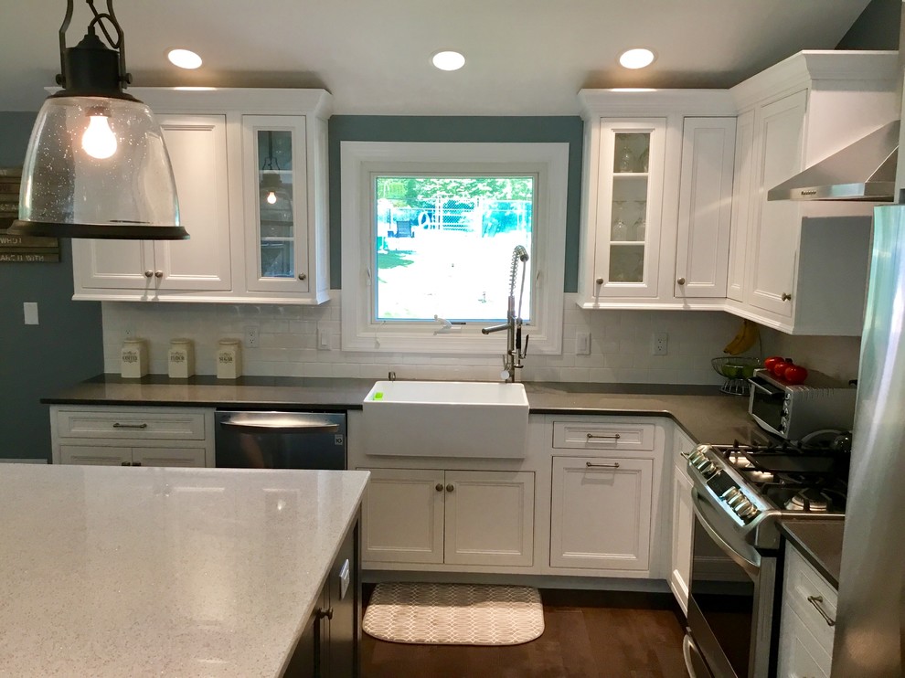 Kitchen - mid-sized transitional l-shaped dark wood floor and brown floor kitchen idea in New York with a farmhouse sink, recessed-panel cabinets, white cabinets, granite countertops, white backsplash, subway tile backsplash, stainless steel appliances, an island and black countertops