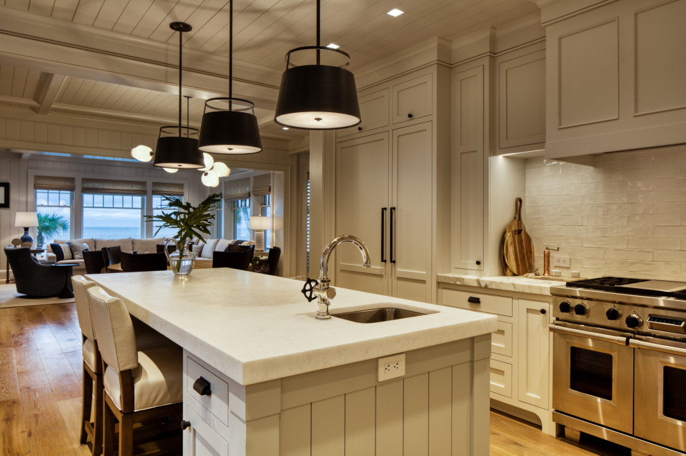 This is an example of a mid-sized beach style kitchen in Jacksonville with a single-bowl sink, recessed-panel cabinets, white cabinets, quartzite benchtops, white splashback, ceramic splashback, stainless steel appliances, light hardwood floors, with island, white benchtop and wood.