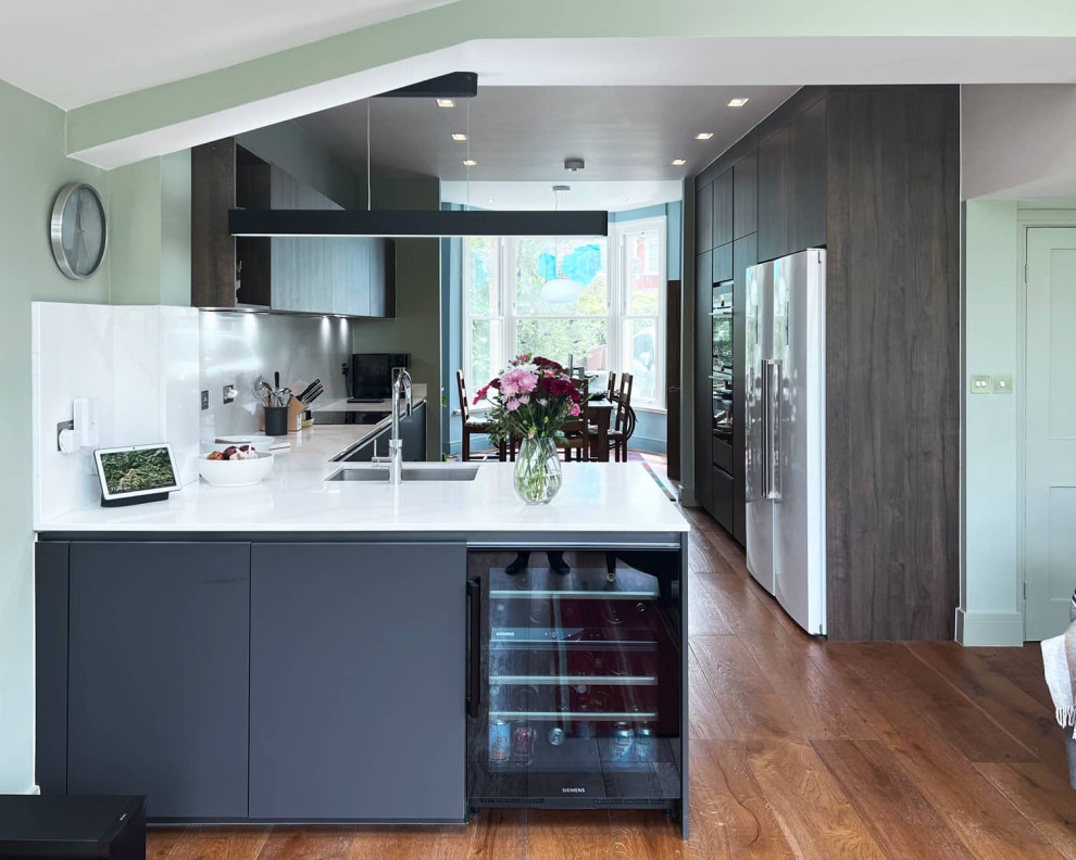 Design ideas for a medium sized contemporary galley kitchen/diner in London with a single-bowl sink, flat-panel cabinets, grey cabinets, quartz worktops, white splashback, black appliances, light hardwood flooring, brown floors and white worktops.