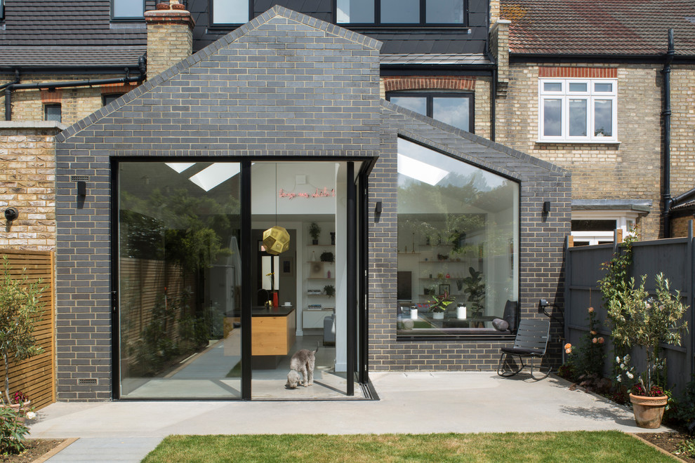 This is an example of a mid-sized contemporary three-storey brick grey townhouse exterior in London with a gable roof and a tile roof.
