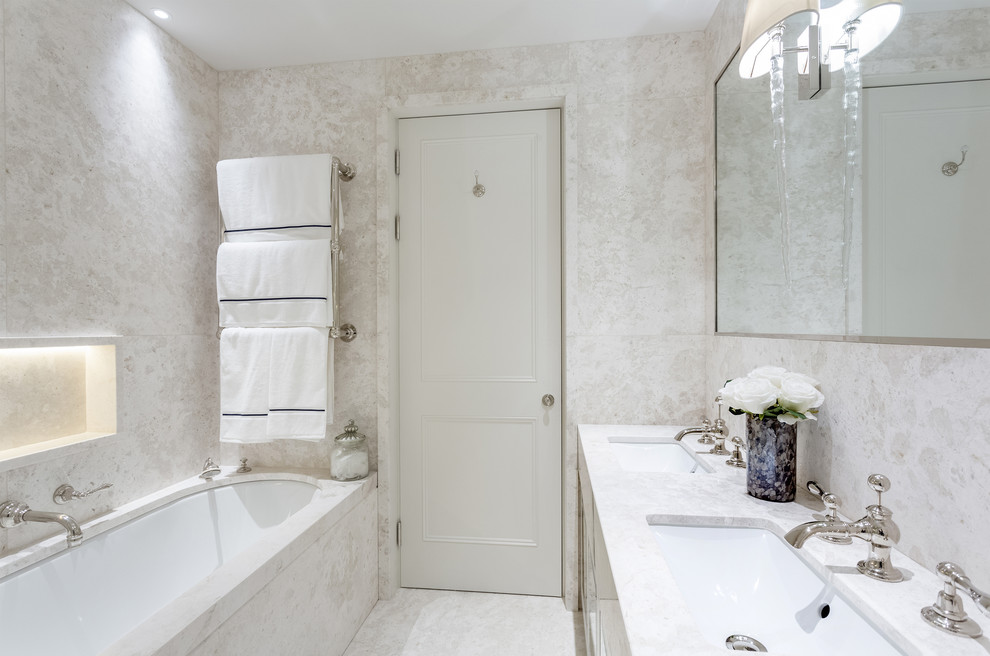 This is an example of a mid-sized contemporary master bathroom in London with white cabinets, a drop-in tub, a corner shower, white tile, marble, white walls, marble floors, an undermount sink, marble benchtops, white floor and a hinged shower door.