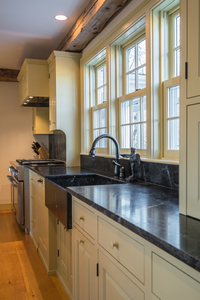 Inspiration for a large cottage single-wall light wood floor eat-in kitchen remodel in Portland Maine with a farmhouse sink, recessed-panel cabinets, white cabinets, soapstone countertops, stone slab backsplash, stainless steel appliances and an island