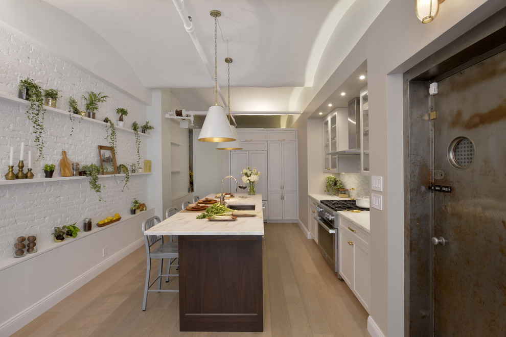 Mid-sized transitional l-shaped light wood floor kitchen photo in New York with an undermount sink, recessed-panel cabinets, marble countertops, glass tile backsplash, paneled appliances, an island, white cabinets and gray backsplash