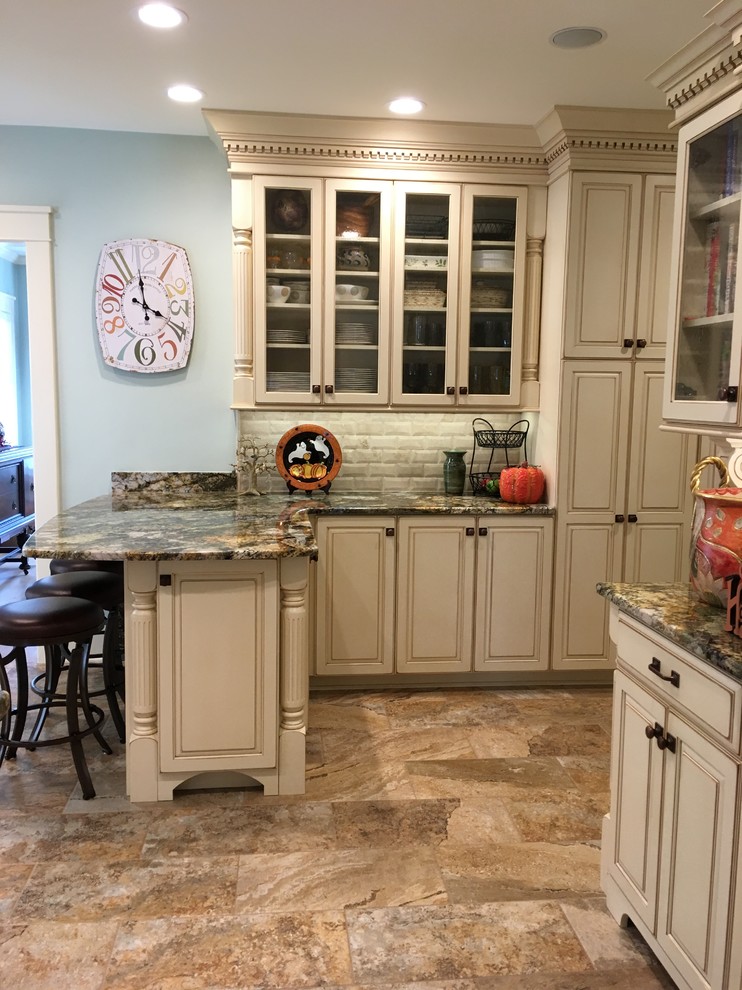 Inspiration for a large transitional galley porcelain tile enclosed kitchen remodel with an undermount sink, raised-panel cabinets, distressed cabinets, granite countertops, beige backsplash, stone tile backsplash, stainless steel appliances and a peninsula