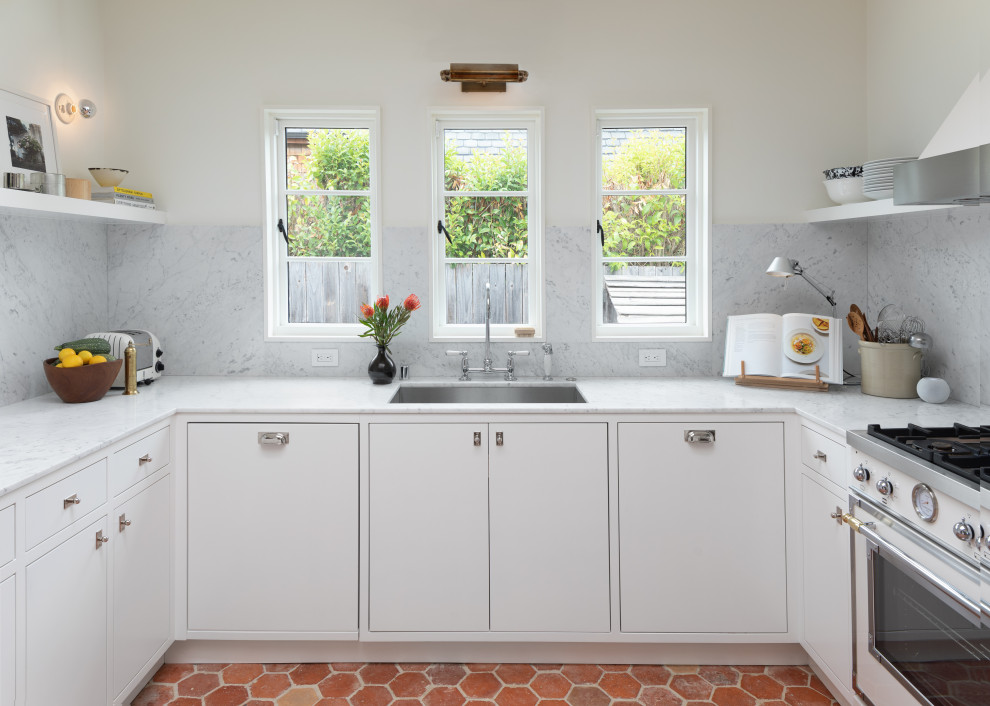 Cette photo montre une cuisine industrielle avec un placard à porte plane, des portes de placard blanches, plan de travail en marbre et tomettes au sol.