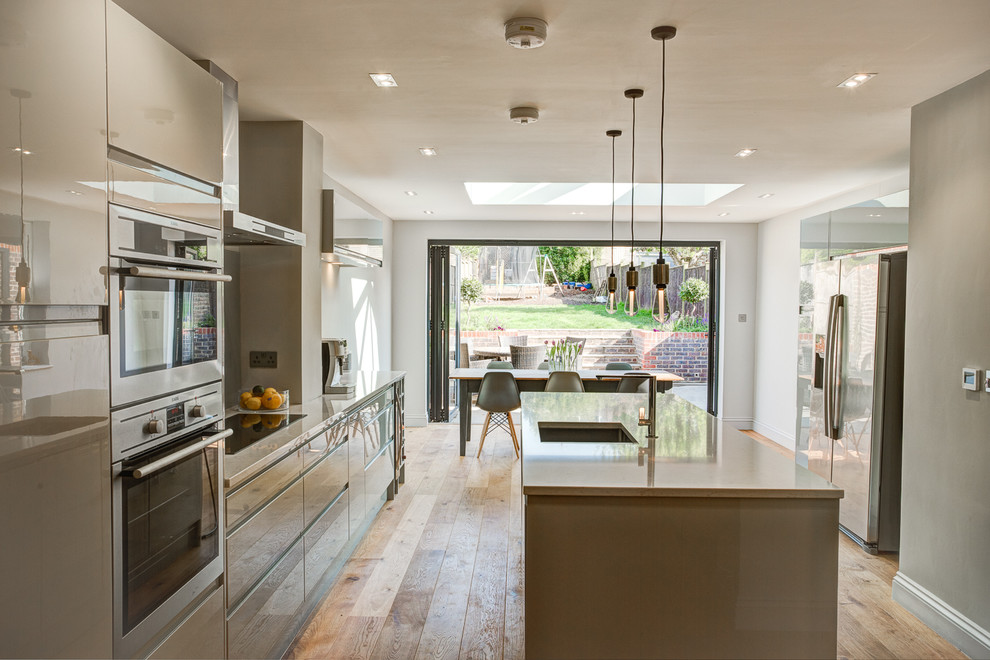 Inspiration for a mid-sized contemporary single-wall eat-in kitchen in Surrey with flat-panel cabinets, grey cabinets, granite benchtops, grey splashback, light hardwood floors, with island, an undermount sink, glass sheet splashback and stainless steel appliances.