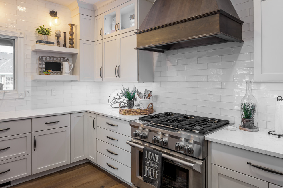 U-shaped brown floor eat-in kitchen photo with a farmhouse sink, shaker cabinets, white cabinets, quartz countertops, white backsplash, subway tile backsplash, stainless steel appliances, an island and white countertops