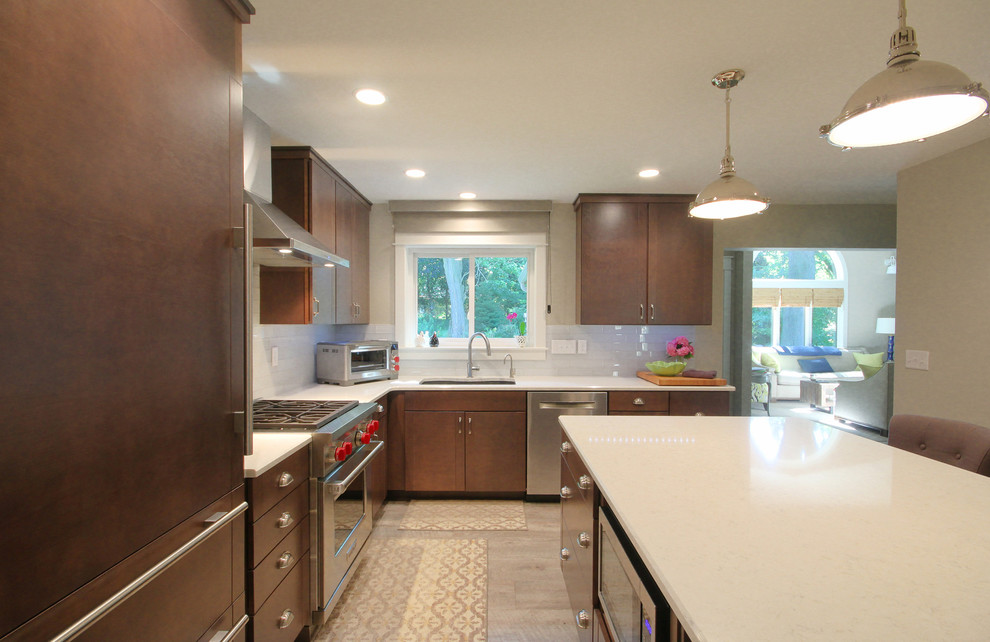 This is an example of a small modern l-shaped eat-in kitchen in Grand Rapids with an undermount sink, flat-panel cabinets, brown cabinets, quartz benchtops, white splashback, subway tile splashback, stainless steel appliances, light hardwood floors and with island.