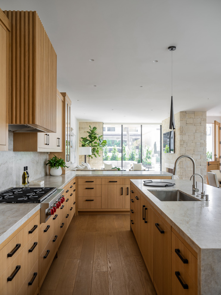 Contemporary l-shaped kitchen in Orange County with an undermount sink, flat-panel cabinets, medium wood cabinets, grey splashback, stone slab splashback, stainless steel appliances, medium hardwood floors, with island, brown floor and grey benchtop.