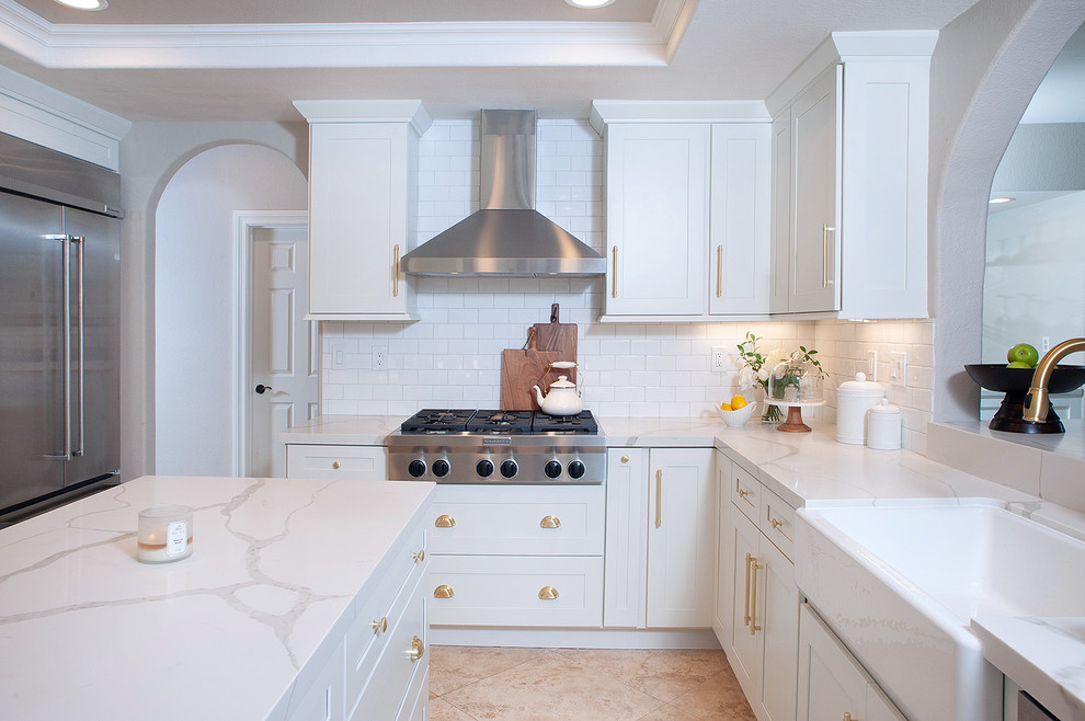 Mid-sized contemporary u-shaped separate kitchen in San Diego with a farmhouse sink, shaker cabinets, white cabinets, quartzite benchtops, white splashback, ceramic splashback, stainless steel appliances, limestone floors, with island, beige floor and white benchtop.