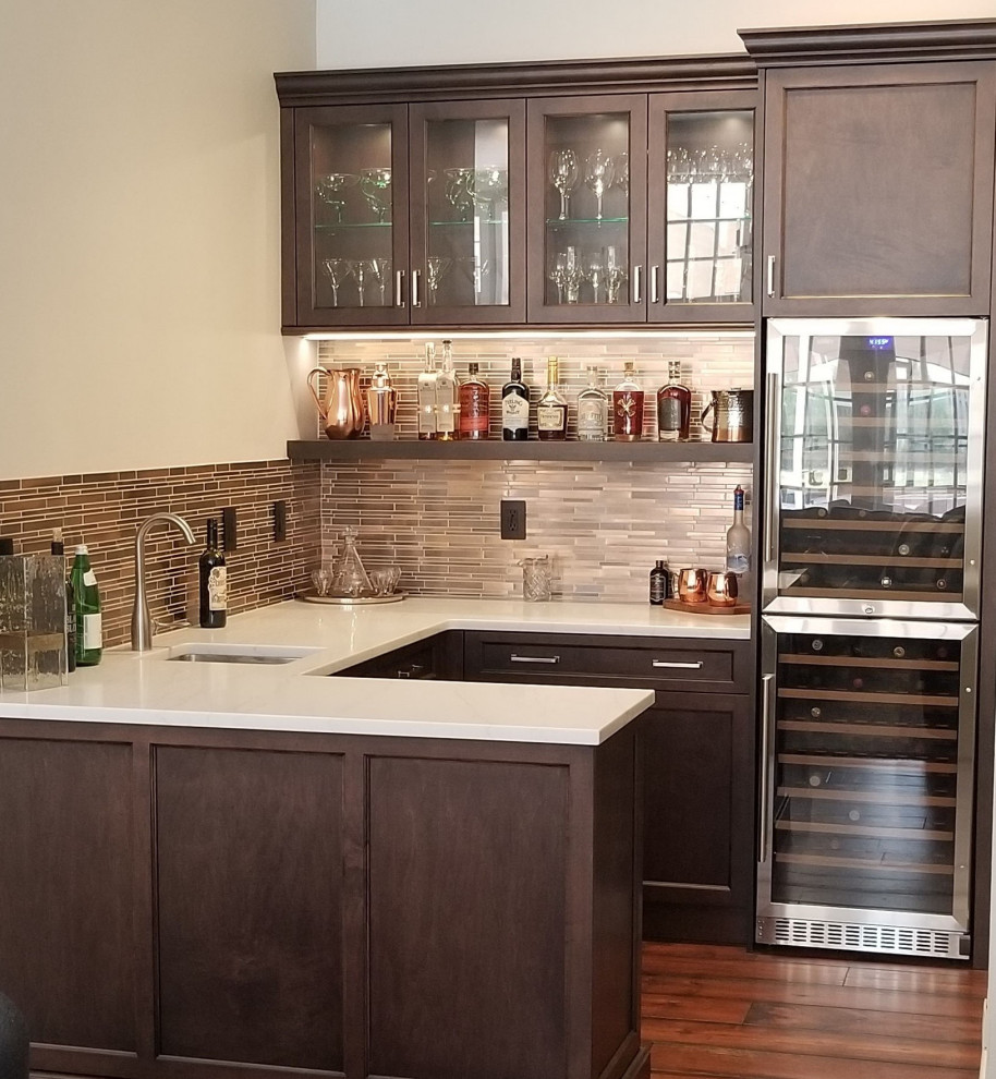 Photo of a small transitional u-shaped wet bar in Tampa with an undermount sink, shaker cabinets, brown cabinets, solid surface benchtops, multi-coloured splashback, medium hardwood floors, brown floor and white benchtop.