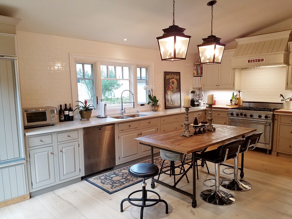 This is an example of a small country l-shaped kitchen in Philadelphia with a double-bowl sink, recessed-panel cabinets, grey cabinets, quartz benchtops, white splashback, subway tile splashback, stainless steel appliances, light hardwood floors, no island and white benchtop.