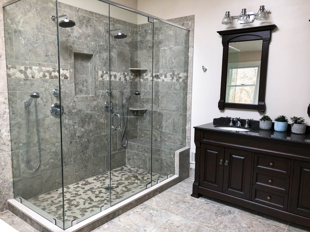 Large transitional master bathroom in Philadelphia with an undermount sink, raised-panel cabinets, dark wood cabinets, granite benchtops, a freestanding tub, a corner shower, a two-piece toilet, gray tile, ceramic tile, beige walls, travertine floors and black benchtops.