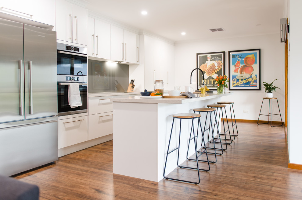 This is an example of a large modern u-shaped kitchen pantry in Melbourne with a double-bowl sink, open cabinets, white cabinets, quartz benchtops, metallic splashback, glass sheet splashback, stainless steel appliances, medium hardwood floors, with island and beige benchtop.