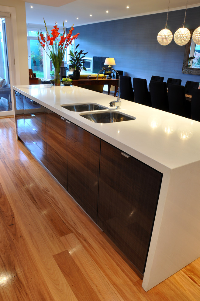 Inspiration for a mid-sized modern l-shaped open plan kitchen in Geelong with an undermount sink, flat-panel cabinets, white cabinets, quartz benchtops, white splashback, glass sheet splashback, stainless steel appliances, light hardwood floors and with island.