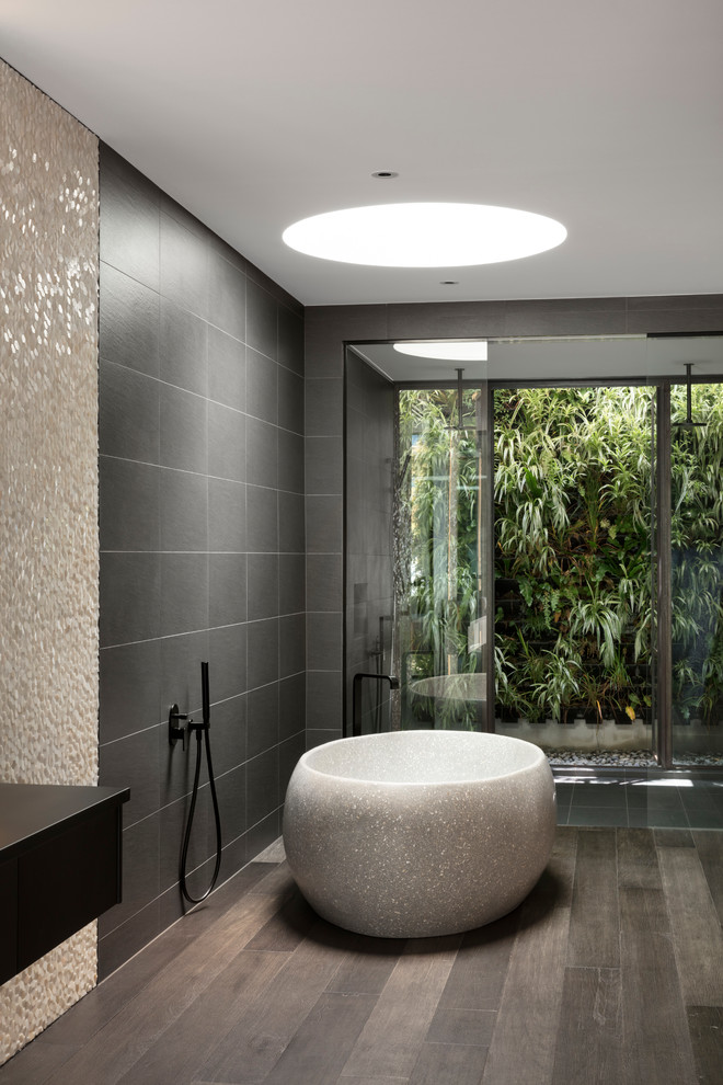 Inspiration for a large contemporary master bathroom in Melbourne with flat-panel cabinets, black cabinets, a freestanding tub, a double shower, gray tile, porcelain tile, dark hardwood floors, a vessel sink, solid surface benchtops, brown floor, an open shower and black benchtops.