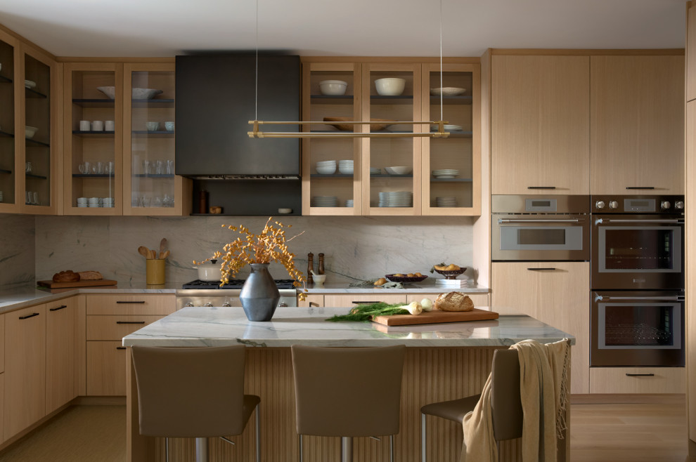 Example of a mid-sized trendy l-shaped light wood floor and beige floor kitchen design with flat-panel cabinets, light wood cabinets, white backsplash, stone slab backsplash, stainless steel appliances, an island and white countertops