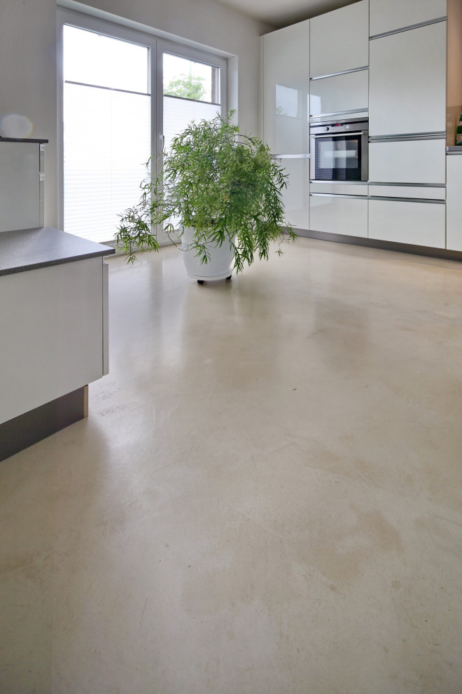 This is an example of an expansive contemporary kitchen in Berlin with white cabinets, concrete floors, a peninsula and beige floor.