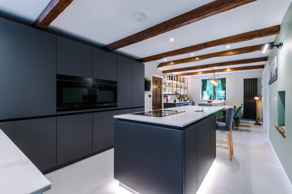 Design ideas for a medium sized contemporary galley open plan kitchen in Manchester with a built-in sink, flat-panel cabinets, grey cabinets, quartz worktops, glass sheet splashback, stainless steel appliances, an island, white worktops and a feature wall.
