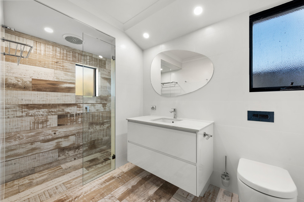 Design ideas for a mid-sized beach style 3/4 bathroom in Perth with flat-panel cabinets, white cabinets, an alcove shower, a one-piece toilet, white tile, ceramic tile, white walls, porcelain floors, an undermount sink, brown floor, an open shower and white benchtops.