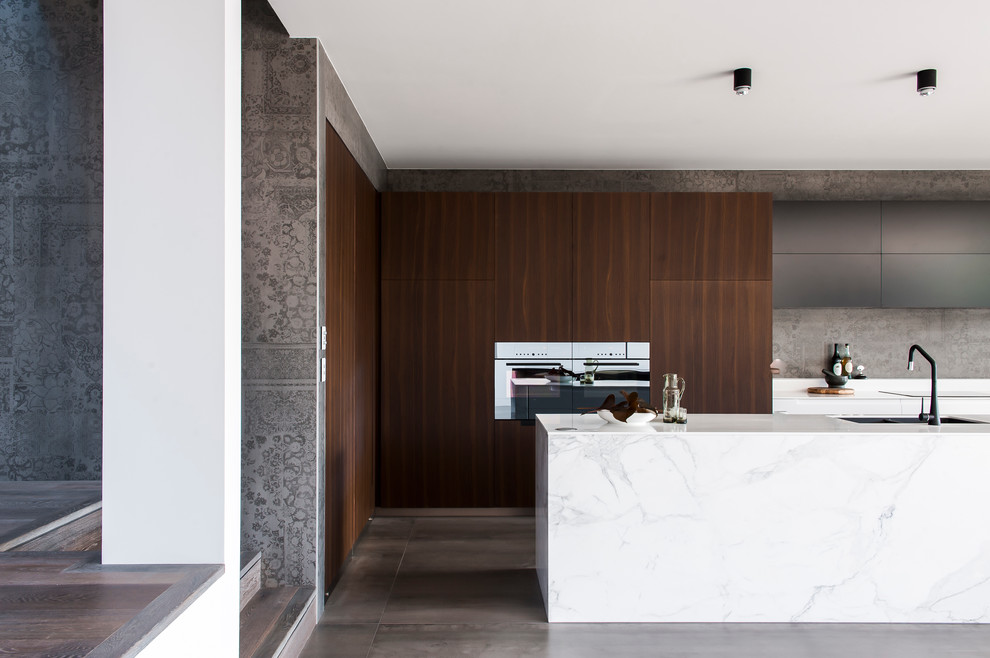 Design ideas for a mid-sized modern l-shaped eat-in kitchen in Sydney with an integrated sink, dark wood cabinets, solid surface benchtops, grey splashback, cement tile splashback, black appliances, ceramic floors and with island.