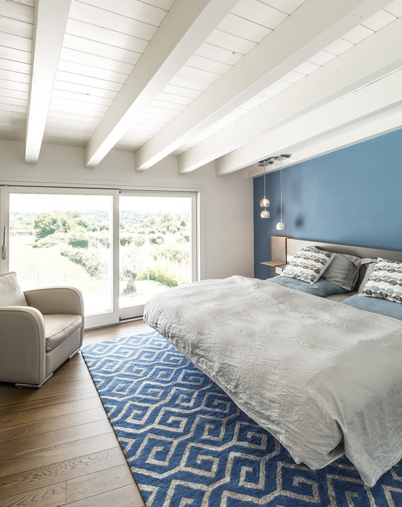 Photo of a mid-sized beach style master bedroom in Milan with blue walls, dark hardwood floors and multi-coloured floor.