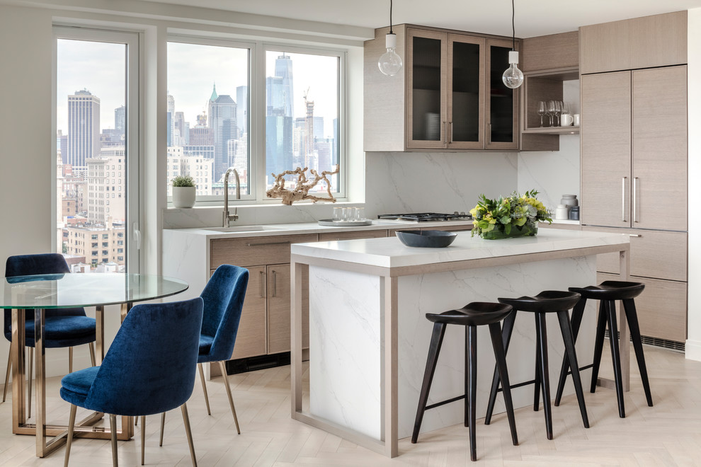 Photo of a mid-sized scandinavian l-shaped eat-in kitchen in New York with glass-front cabinets, light wood cabinets, marble benchtops, white splashback, marble splashback, panelled appliances, light hardwood floors, with island, beige floor, white benchtop and an undermount sink.