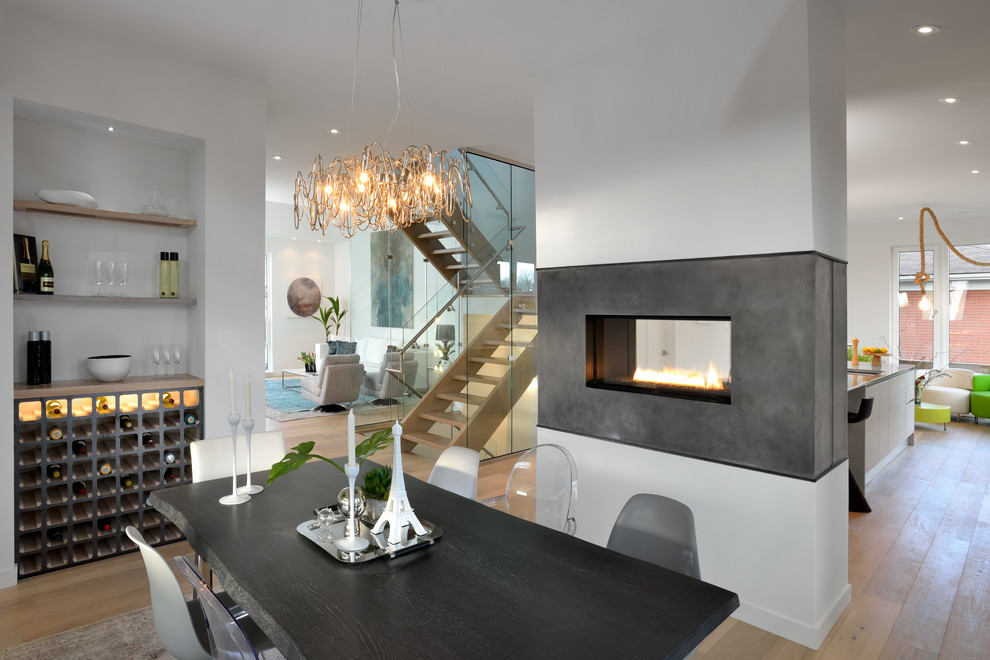 This is an example of a mid-sized contemporary separate dining room in Toronto with white walls, light hardwood floors, a two-sided fireplace, a concrete fireplace surround and beige floor.