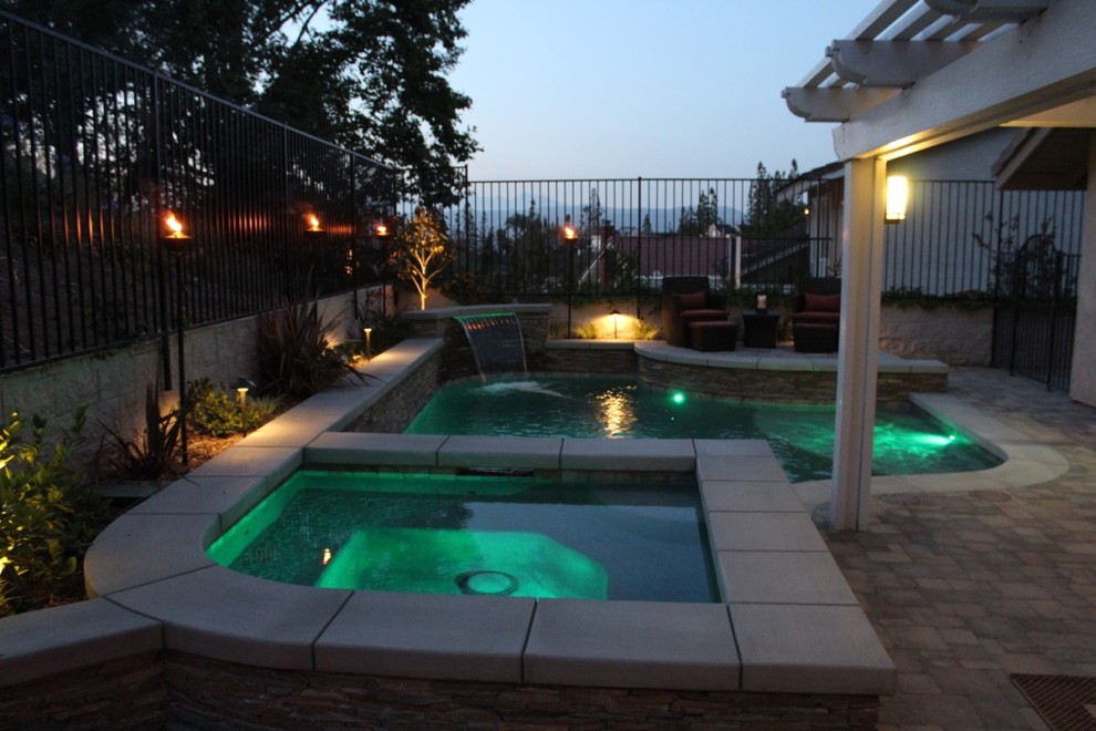 Design ideas for a mid-sized traditional backyard custom-shaped pool in Orange County with a water feature and concrete pavers.