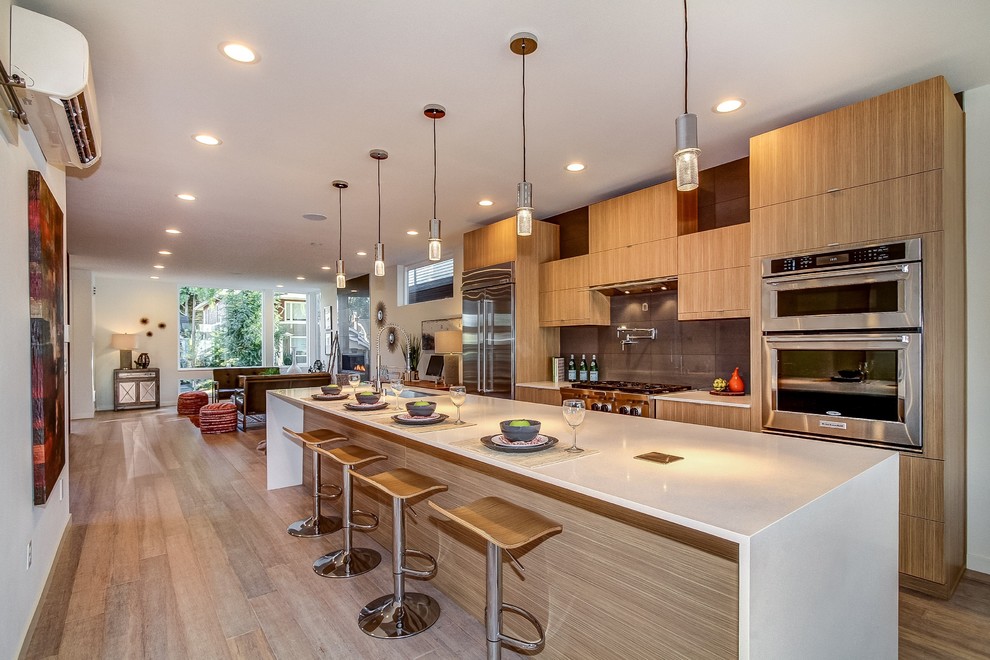 Photo of a contemporary galley kitchen in Seattle with flat-panel cabinets, medium wood cabinets, grey splashback, stainless steel appliances, light hardwood floors, with island, beige floor and white benchtop.