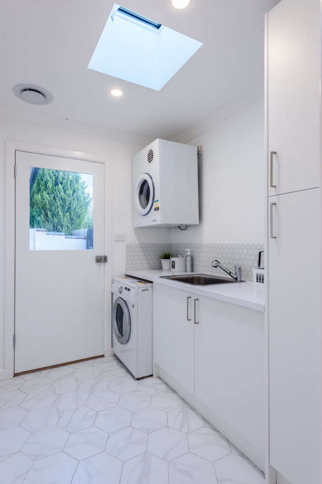 Small modern utility room in Other with an integrated washer and dryer, a single-bowl sink, white cabinets, quartz benchtops, grey splashback, ceramic splashback, white walls, laminate floors, multi-coloured floor and white benchtop.