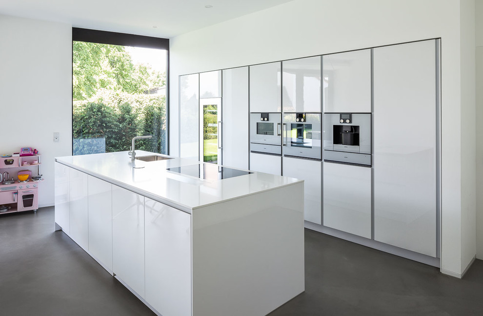Large contemporary galley open plan kitchen in Cologne with an undermount sink, flat-panel cabinets, white cabinets, quartz benchtops, white splashback, white appliances and with island.