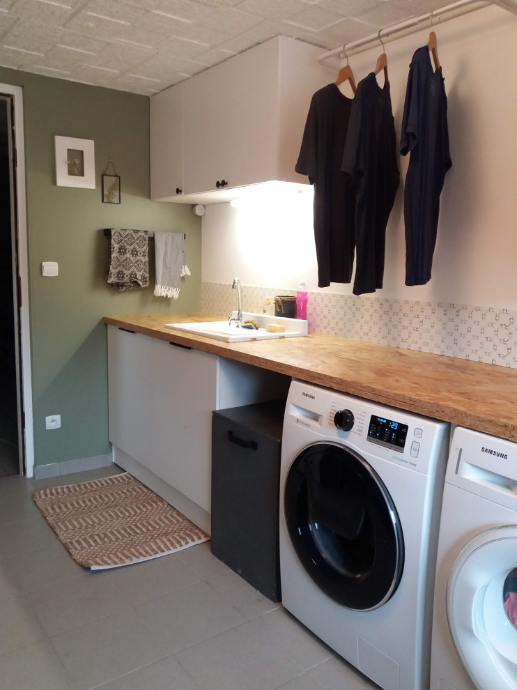 Ispirazione per una sala lavanderia scandinava di medie dimensioni con lavello sottopiano, top in legno, paraspruzzi verde, pareti verdi, lavatrice e asciugatrice affiancate e pavimento grigio