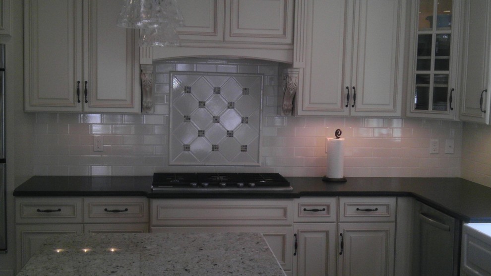 Example of a mid-sized l-shaped light wood floor eat-in kitchen design in Newark with a drop-in sink, raised-panel cabinets, white cabinets, granite countertops, white backsplash, subway tile backsplash, stainless steel appliances and an island