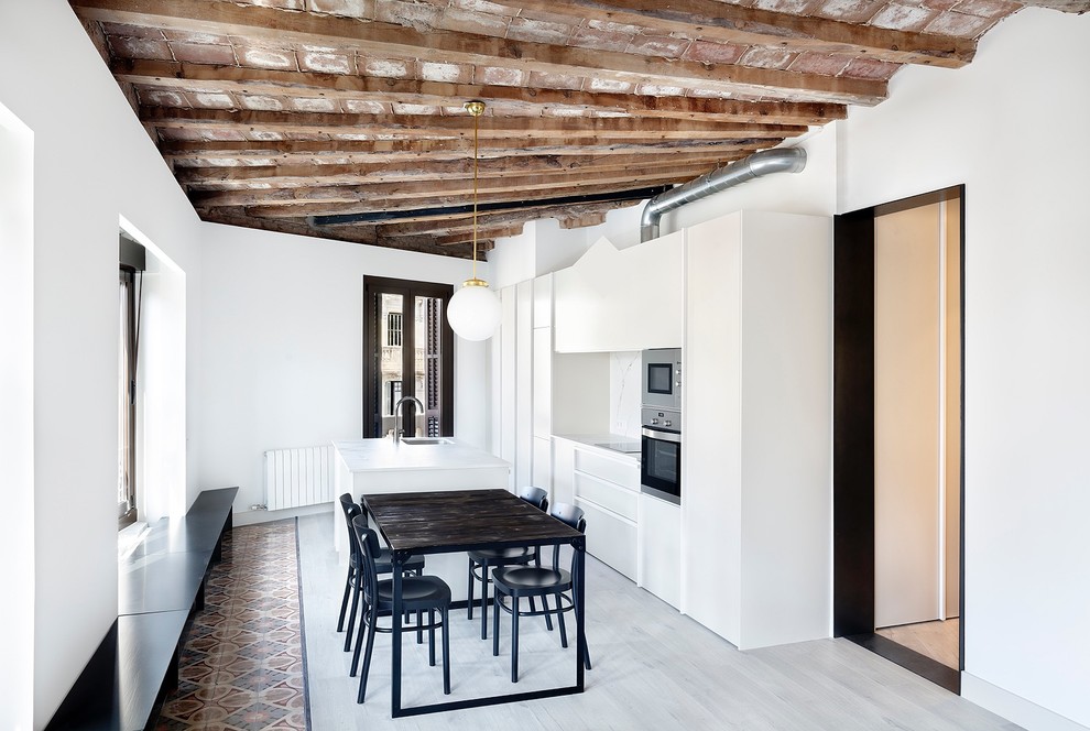 This is an example of a contemporary single-wall eat-in kitchen in Barcelona with an undermount sink, flat-panel cabinets, white cabinets, white splashback, stainless steel appliances, light hardwood floors, with island and grey floor.