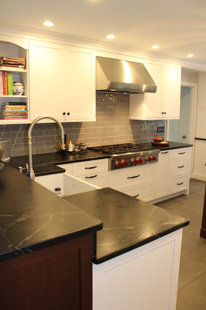 Large traditional u-shaped eat-in kitchen in Boston with a farmhouse sink, recessed-panel cabinets, white cabinets, granite benchtops, grey splashback, subway tile splashback, stainless steel appliances, porcelain floors, with island, grey floor and black benchtop.