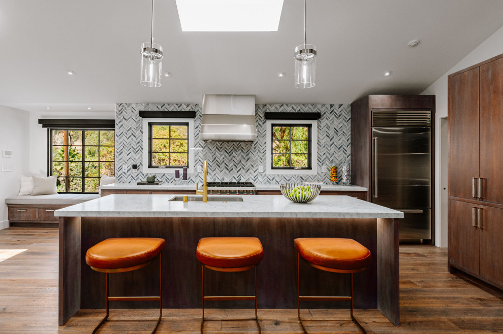 Expansive country single-wall open plan kitchen in Los Angeles with an undermount sink, recessed-panel cabinets, dark wood cabinets, marble benchtops, matchstick tile splashback, stainless steel appliances, medium hardwood floors, with island and grey benchtop.