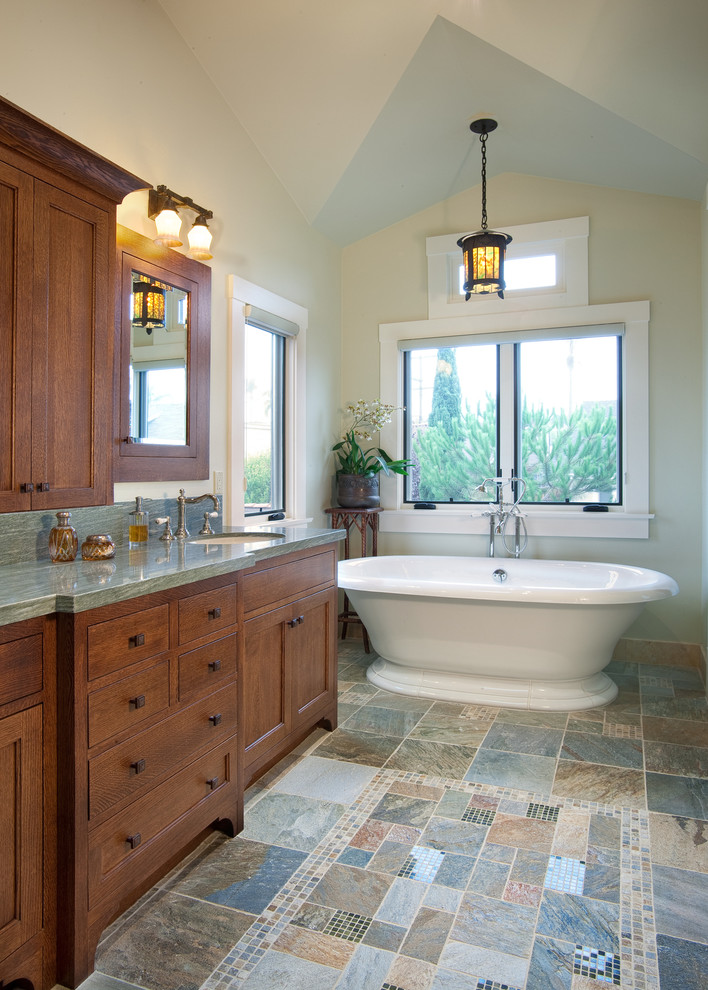 Large arts and crafts master bathroom in San Diego with recessed-panel cabinets, medium wood cabinets, a freestanding tub, beige walls, an undermount sink, granite benchtops, slate floors, gray tile, stone slab, a two-piece toilet and multi-coloured floor.