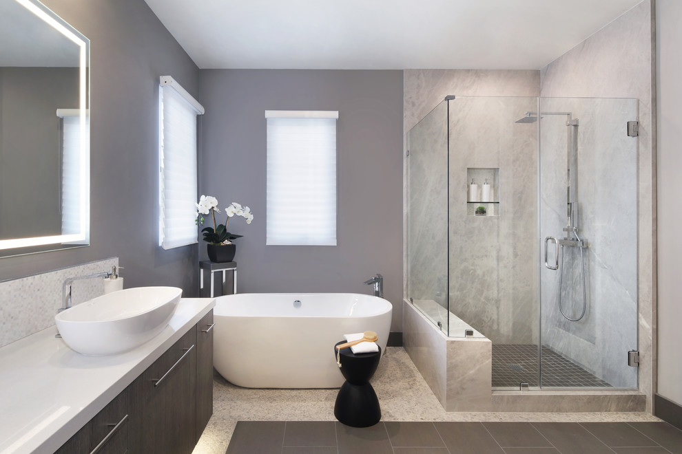 Mid-sized modern master bathroom with flat-panel cabinets, dark wood cabinets, a freestanding tub, a corner shower, gray tile, stone slab, grey walls, porcelain floors, a vessel sink, engineered quartz benchtops, grey floor, a hinged shower door and white benchtops.