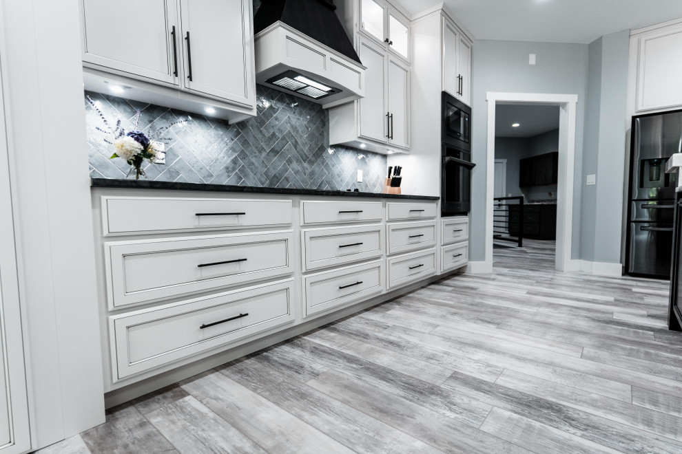Inspiration for a huge transitional l-shaped laminate floor, gray floor and tray ceiling open concept kitchen remodel with an undermount sink, flat-panel cabinets, white cabinets, quartz countertops, gray backsplash, ceramic backsplash, black appliances and an island