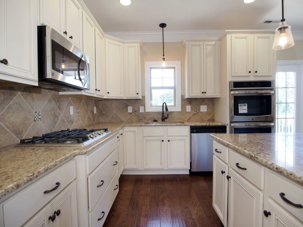 Inspiration for a mid-sized transitional l-shaped eat-in kitchen in Raleigh with a double-bowl sink, beaded inset cabinets, white cabinets, granite benchtops, beige splashback, porcelain splashback, stainless steel appliances, medium hardwood floors, with island, brown floor and multi-coloured benchtop.